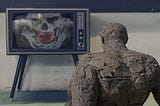stone statue of a person leans back in front of old-style TV with a zombie clown on the screen