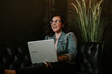 A female user smiling on a leather couch and testing a digital product on her laptop.