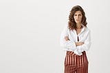 Middle-aged woman wearing a white shirt and stripey trousers looking mad.