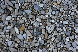 A pile of stones like you would find on the bottom of a creek bed. One of the stones has a question mark hand written in black marker.