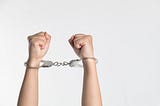 A person’s two raised fisted hands in handcuffs