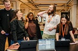 A group of coding bootcamp learners stood around laptops laughing.