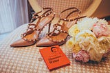 An array of beautiful shoes and flowers surround a small book with the title “How to be a Glamorous Writer.”