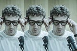 A still repeated three times shows Mark Zuckerberg putting on a pair of Meta glasses. A caption reads “I mean, this is basically what the interaction looks like.”
