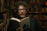 Neil Gaiman reading from one of his short stories to audience. He is wearing Black t-shirt with black suit.