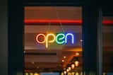 An ‘open’ sign on a shop window in rainbow colours