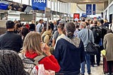 Large crowd of people standing in lineups at an airport gate.