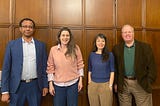 Four speakers standing against a brown paneled wall.