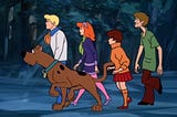 The Scooby-Doo Mystery Gang (including Fred, Scooby, Daphne, Velma, and Shaggy) walking through the woods.