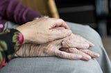 A woman’s hand covers the wrinkled hand of her elderly mother.