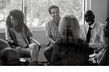 A diverse looking group of people sitting in a circle, apparently in an office setting.