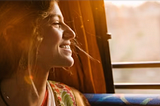An India woman looking out of the window in a moving bus and smiling