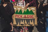 Poster being carried in a crowd, labelled “PICK A SIDE”