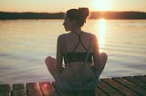 How you can cultivate a growth mindset and create a better life for yourself and everyone else. Image: A woman sitting on a dock at sunset.
