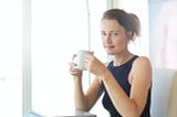 woman smiling as she holds a cup of coffee while pausing at her desk