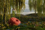 A rusty red beanbag chair underneath a white reading lamp set in a grassy field of flowers with willow tree branches draping around