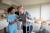 Home health aide helps an old man on a crutch