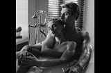 Man and woman sitting in a tub. He is embracing her from behind.