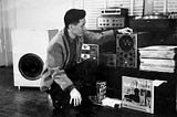 A man crouching down while looking at analog stereos and vinyl records