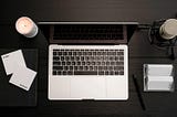 Macbook, sticky notes, microphone and a burning candle on a black desk