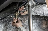 Photo of a worker’s hands fixing plumbing against a gray background.