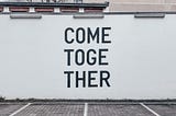 White wall in Berlin, black letters on wall that say “Come Together”