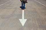 Man standing on arrow sign (photo by Smart on Unsplash)