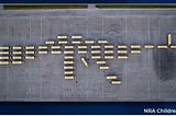 fifty two yellow schools buses arranged in the shape of an AR-15 assault weapon; one bus represents the trigger, and another represents the front sight