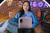 A Woman Recording Herself with a Smartphone while eating a slice of pizza