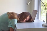 A bored girl lying on a her laptop on a white desk on a sunny morning