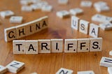 Scrabble tiles standing on edge, spelling out TARIFFS, CHINA, and USA.
