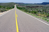 An asphalt road with a yellow line down the middle stretches to the horizon.