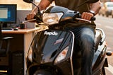 A confident 25-year-old in casual Indian attire sitting on a motorcycle, wearing a focused expression, representing the duality of an IT professional who pursues his passion for driving on the side. The background blends an office environment with city roads, symbolizing the balance between security and passion.
