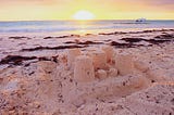 A sandcastle on a beach with the sun setting in the background.