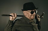 Stylish older man in hat and sunglasses holding cane across shoulders