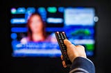 A hand holding a television remote while switching to a news channel