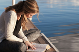 A woman sits on a dock, reading a book.