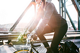 a woman rides a bike over a metal bridge. the sun is shining brightly