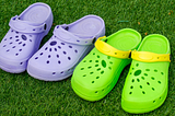 Pair of purple and green crocs on some grass