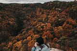 woman at the top of a mountain peak gazing out over foliage