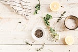 A white, reclaimed wood table, with a variety of bundled herbs, and dried herbs in simple but elegant pots.