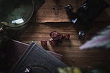 A set of D&D dice on a wooden table surrounded by leather-bound books and other assorted dice