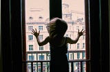 Woman pushing against a window, looking across at an old street.