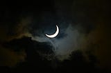 Crescent moon behind a thin cloud.