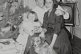 1950s-era couple with child and dog in front of TV and Christmas tree.