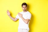 Man showing kung-fu skills, standing in white t-shirt on a yellow background.