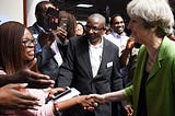 Former Prime Minister Theresa May shaking hands with Jesus House representatives, with press surrounding them.