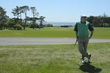 Eric leaning on a club at Pebble Beach, ocean in the background