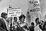 Civil Rights marchers holding signs that say “ Segregated schools must stop now” and Police brutality must stop.” Circa 1960s
