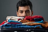 A man staring at a suitcase so packed it cannot be closed.